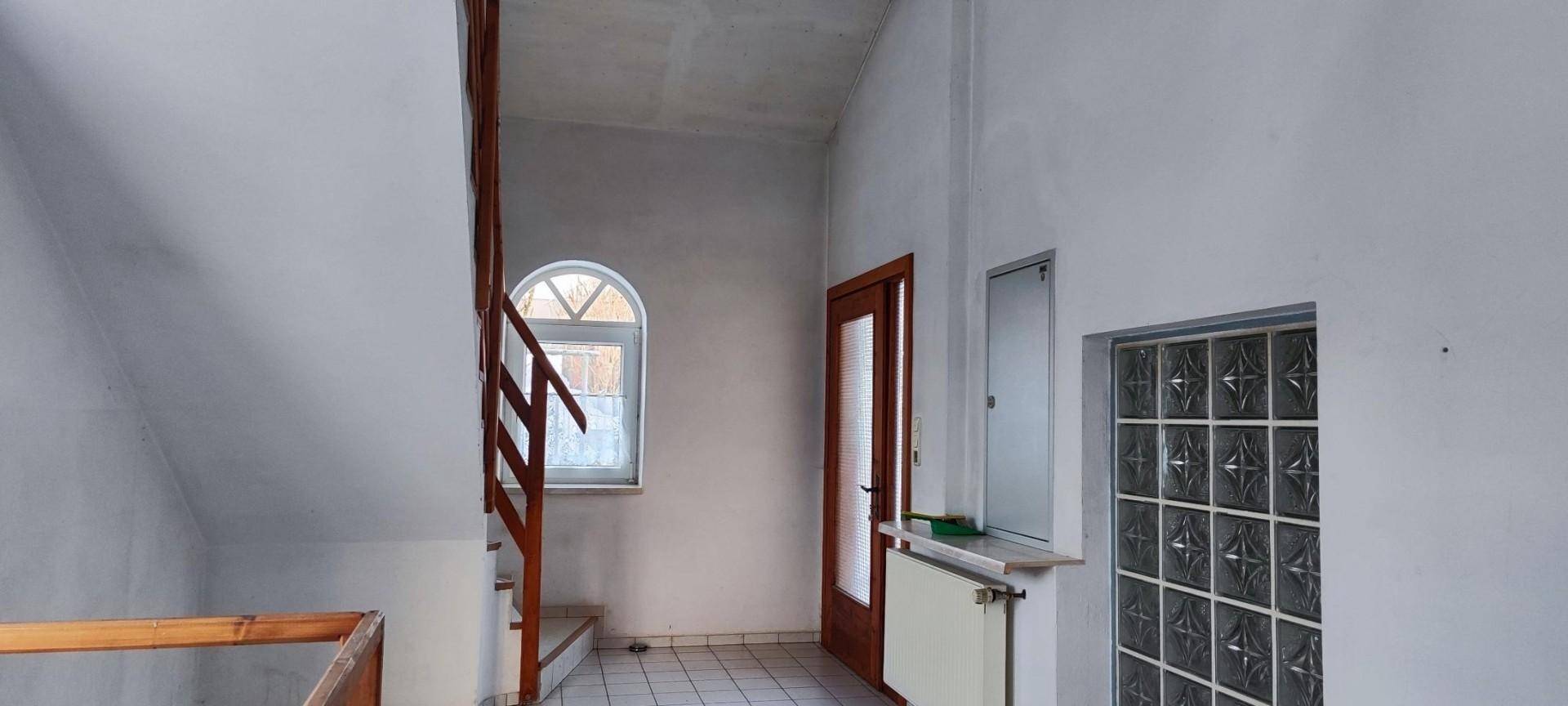 Treppenhaus mit Holzgeländer, Rundbogenfenster und weiß gestrichenen Wänden.