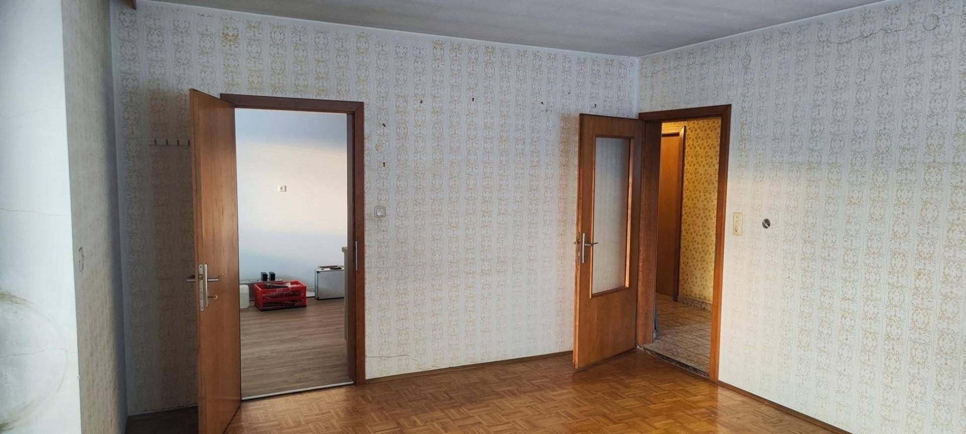 Geräumiges Zimmer mit gemusterter Tapete, Parkettboden und Holztüren.