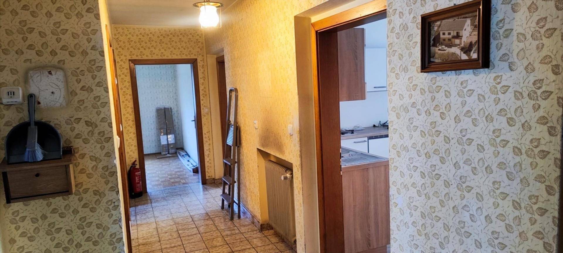 Flur mit gemusterter Tapete, Fliesenboden und Zugang zu verschiedenen Räumen.