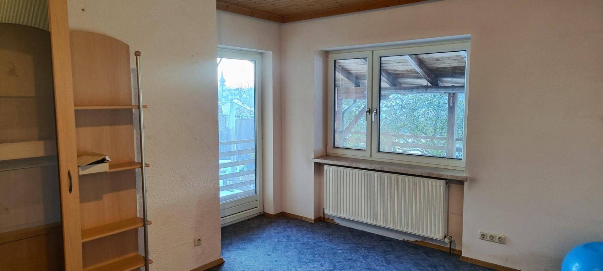 Helles Zimmer mit Fenster, Zugang zum Balkon und Teppichboden.