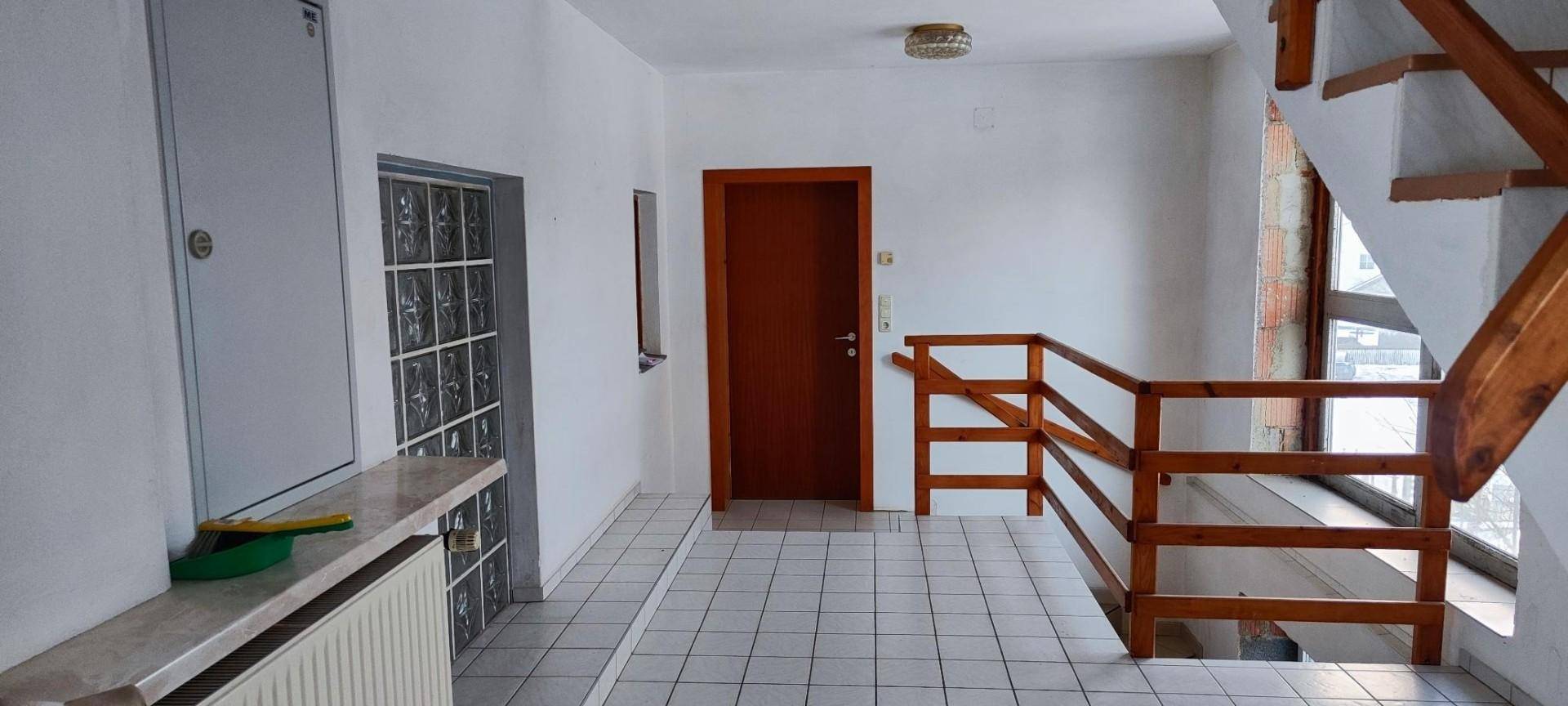 Heller Flur mit weißem Fliesenboden, Holztreppe und Zugang zu weiteren Etagen.