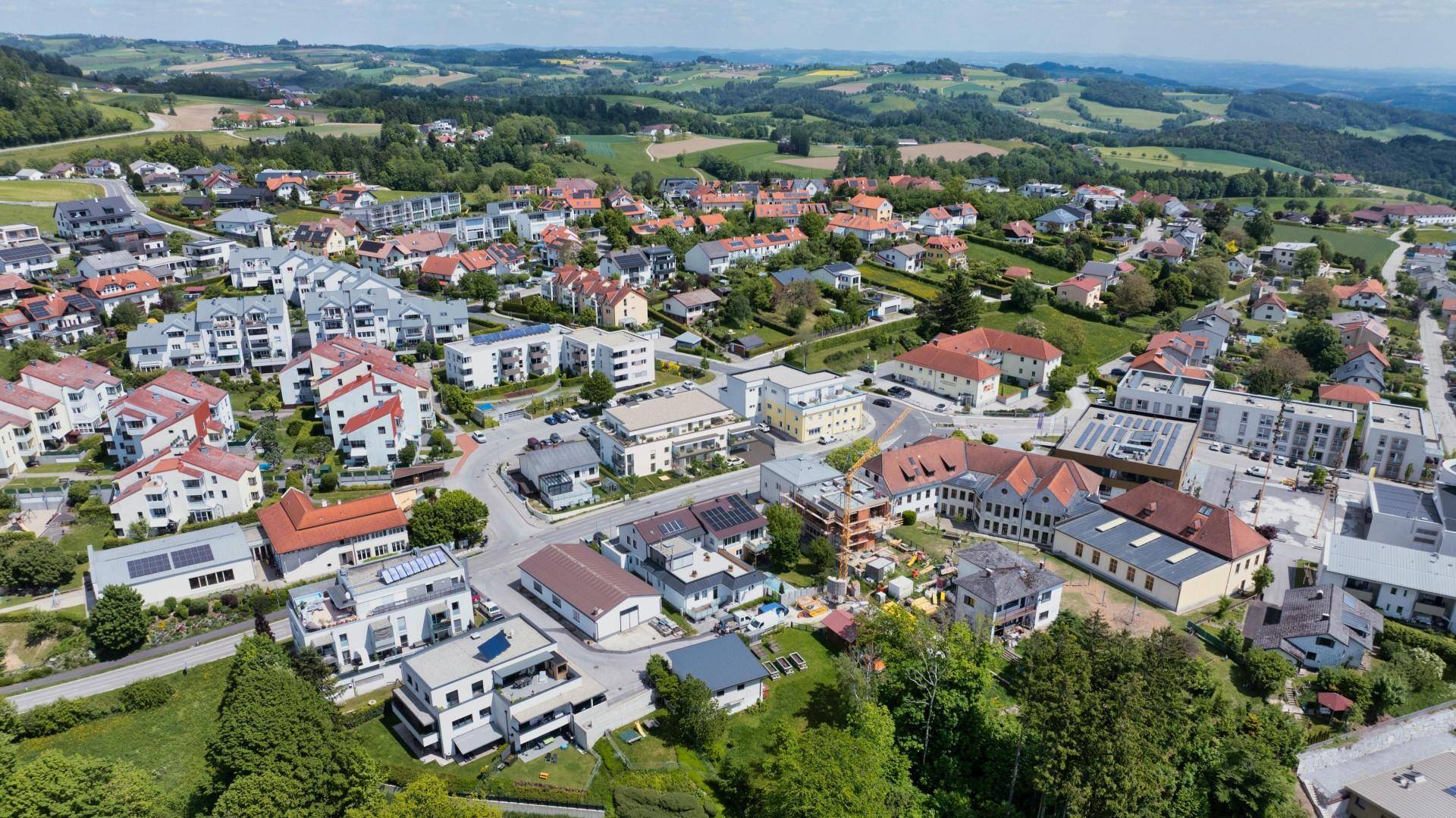 Luftaufnahme einer Wohnsiedlung mit vielen Häusern und grünen Hügeln in der Umgebung.