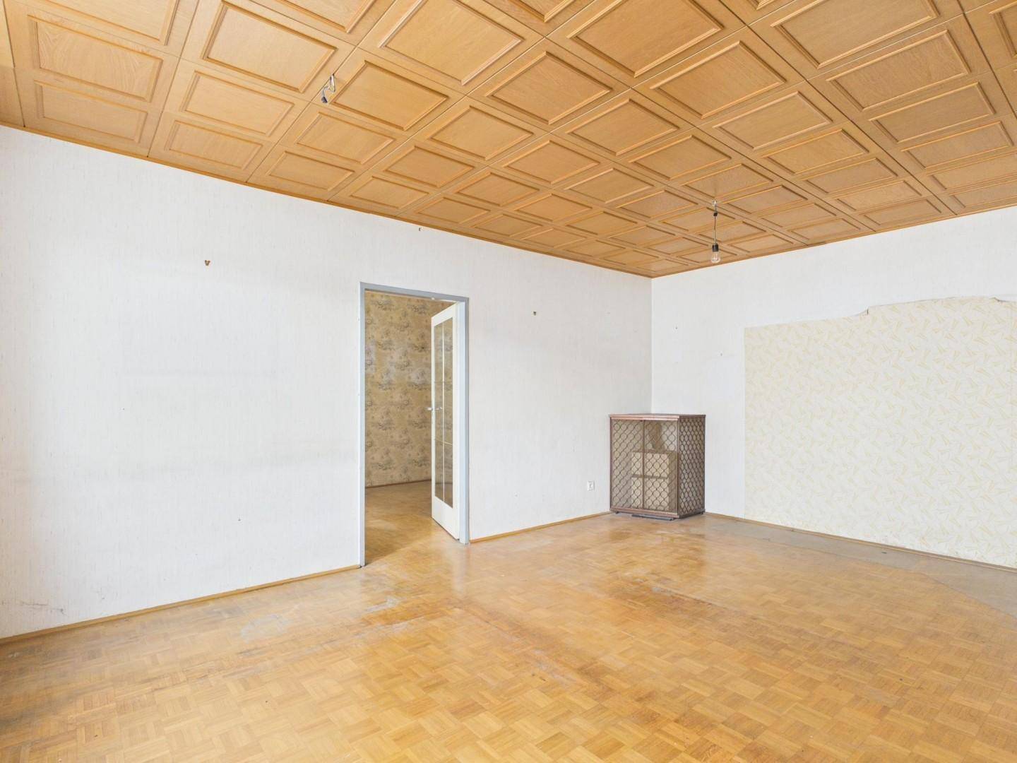 Leeres Wohnzimmer mit Fischgrätparkettboden und einer Holzpaneeldecke, bereit zur Renovierung.