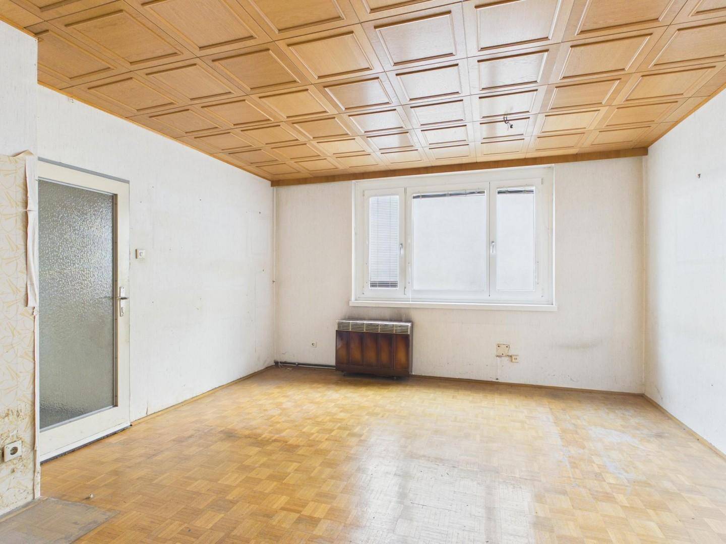 Helles Zimmer mit Parkettboden, Holzpaneeldecke und Fenster, das auf eine Renovierung wartet.
