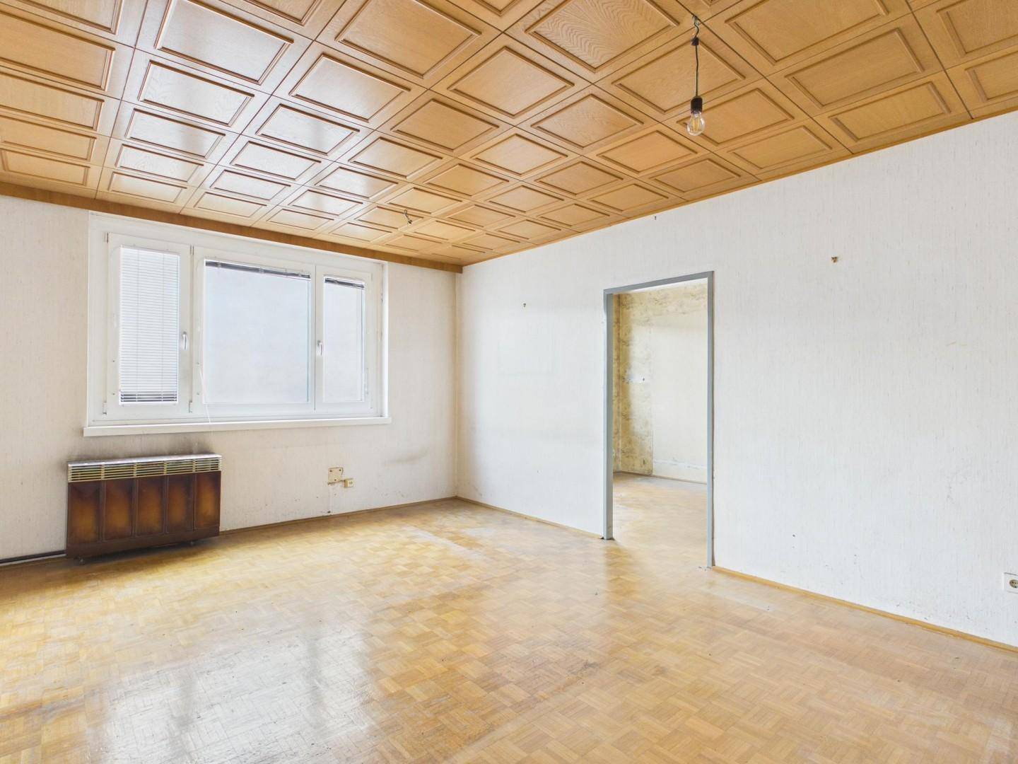 Geräumiges Zimmer mit Parkettboden und Holzpaneeldecke, das viel Potenzial für eine Modernisierung bietet.