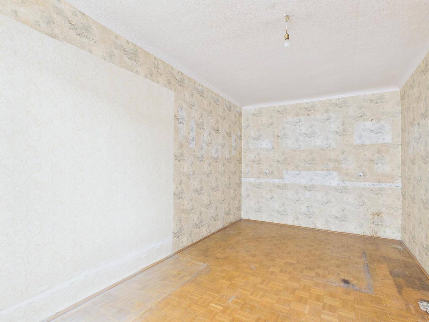 Leeres Zimmer mit gemusterter Tapete und Parkettboden, das auf eine Neugestaltung wartet.