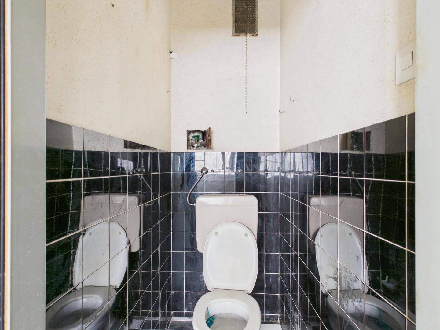 Toilette mit schwarzen Fliesen und einem einfachen WC, das eine Renovierung benötigt.