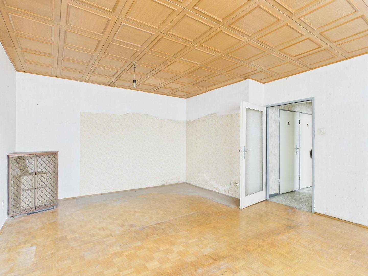 Geräumiges Wohnzimmer mit Holzparkett und Kassettendecke, das auf eine Modernisierung wartet.
