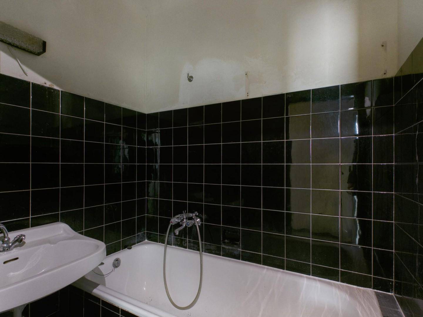 Badezimmer mit schwarzen Fliesen, einer Badewanne und einem Waschbecken, das renoviert werden muss.