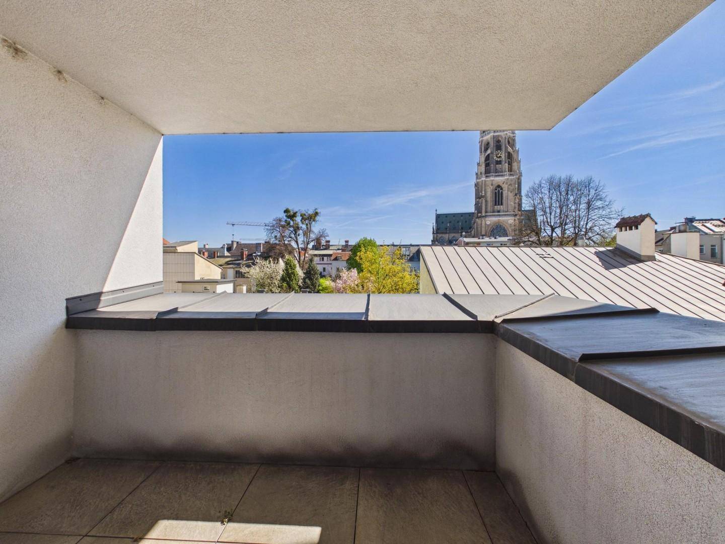 Kleiner Balkon mit Blick auf die Dächer der Stadt und einen Kirchturm im Hintergrund.