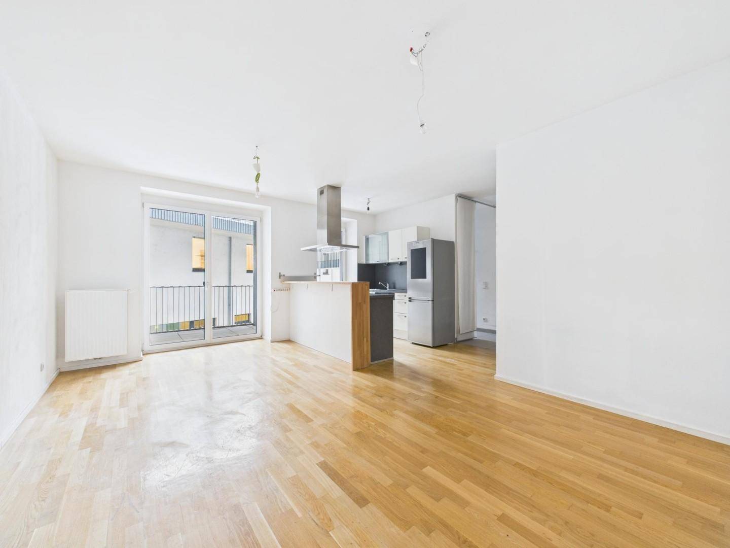 Heller offener Wohnbereich mit Parkettboden und integrierter Küche, mit Zugang zum Balkon.