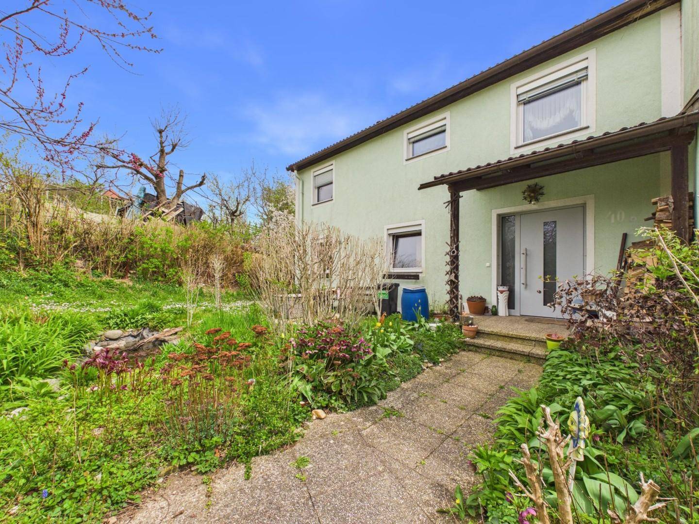 Einfamilienhaus mit hellgrüner Fassade und einem naturnahen Vorgartenbereich.