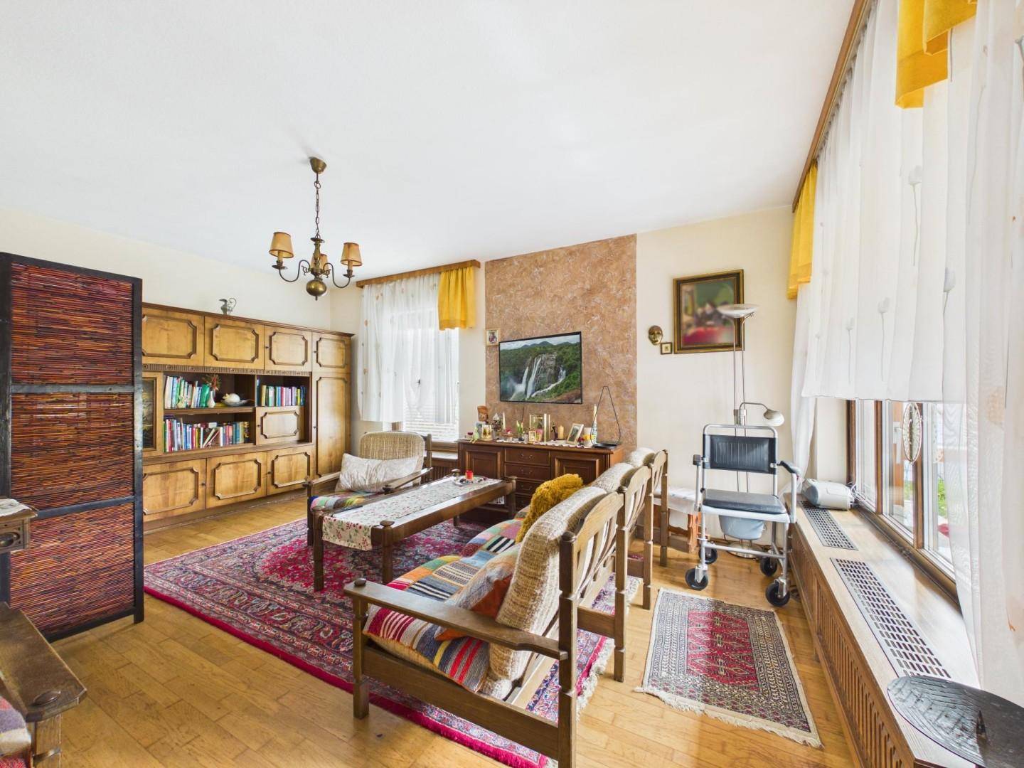 Geräumiges Wohnzimmer mit traditionellen Holzmöbeln, Parkettboden und großen Fenstern.