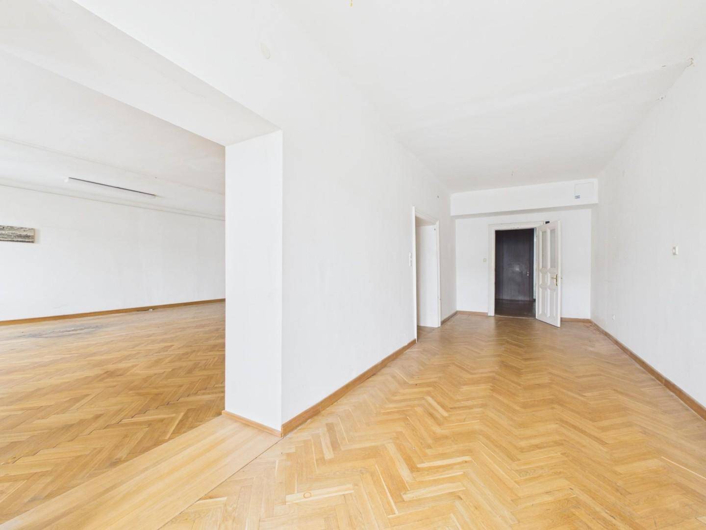 Geräumiger, leerer Raum mit Fischgrätparkett und einem breiten Durchgang zu einem weiteren Zimmer.