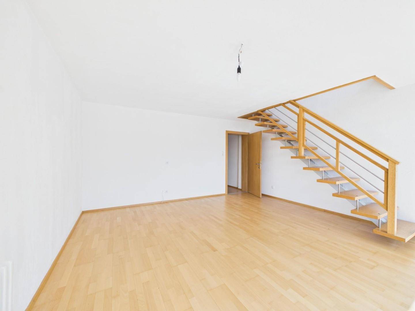 Geräumiger, heller Raum mit Holzparkett und offener Holztreppe, die in eine obere Etage führt.