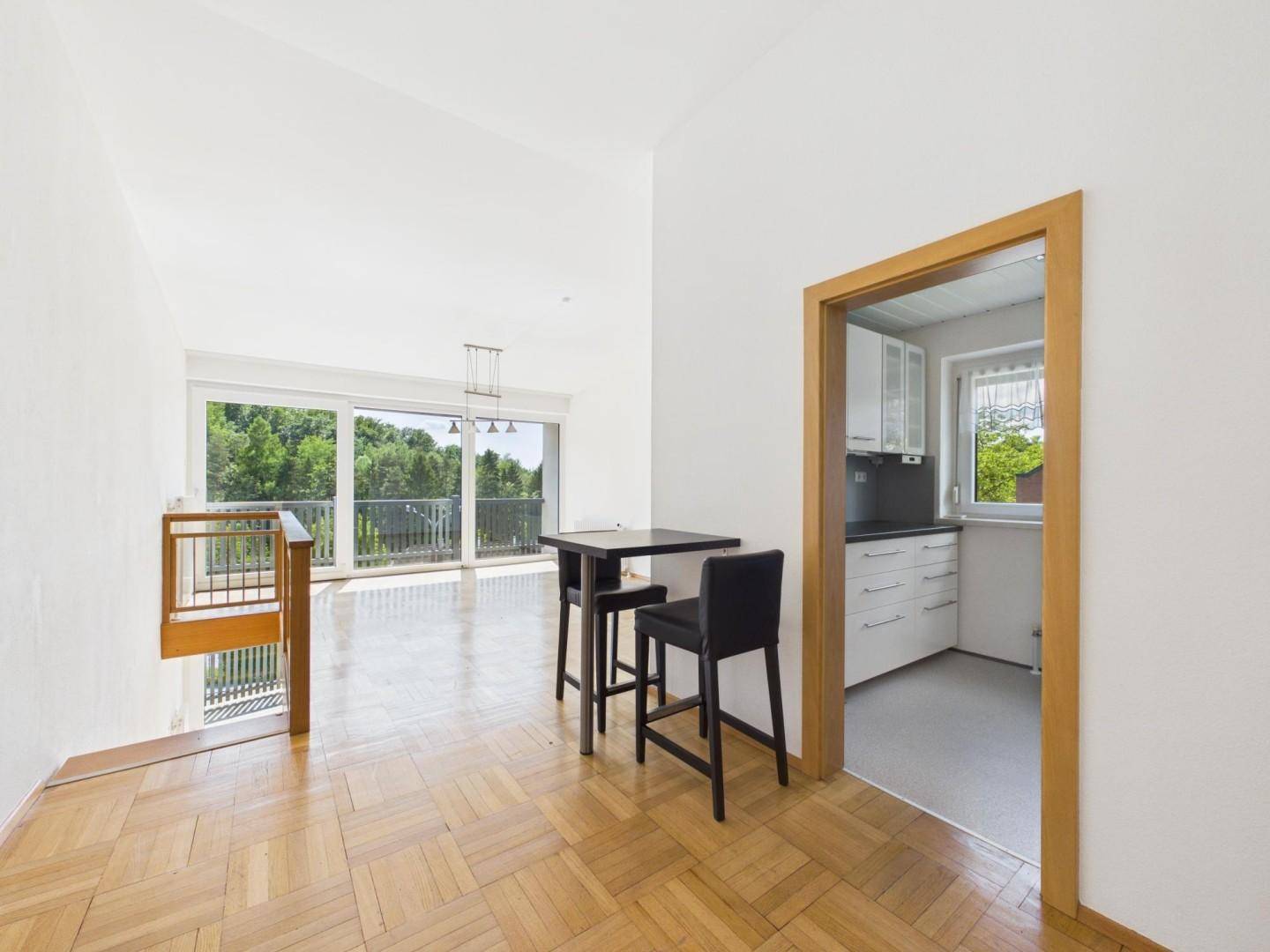 Offener Wohn- und Essbereich mit Parkettboden, Bartisch und Blick auf den Balkon.