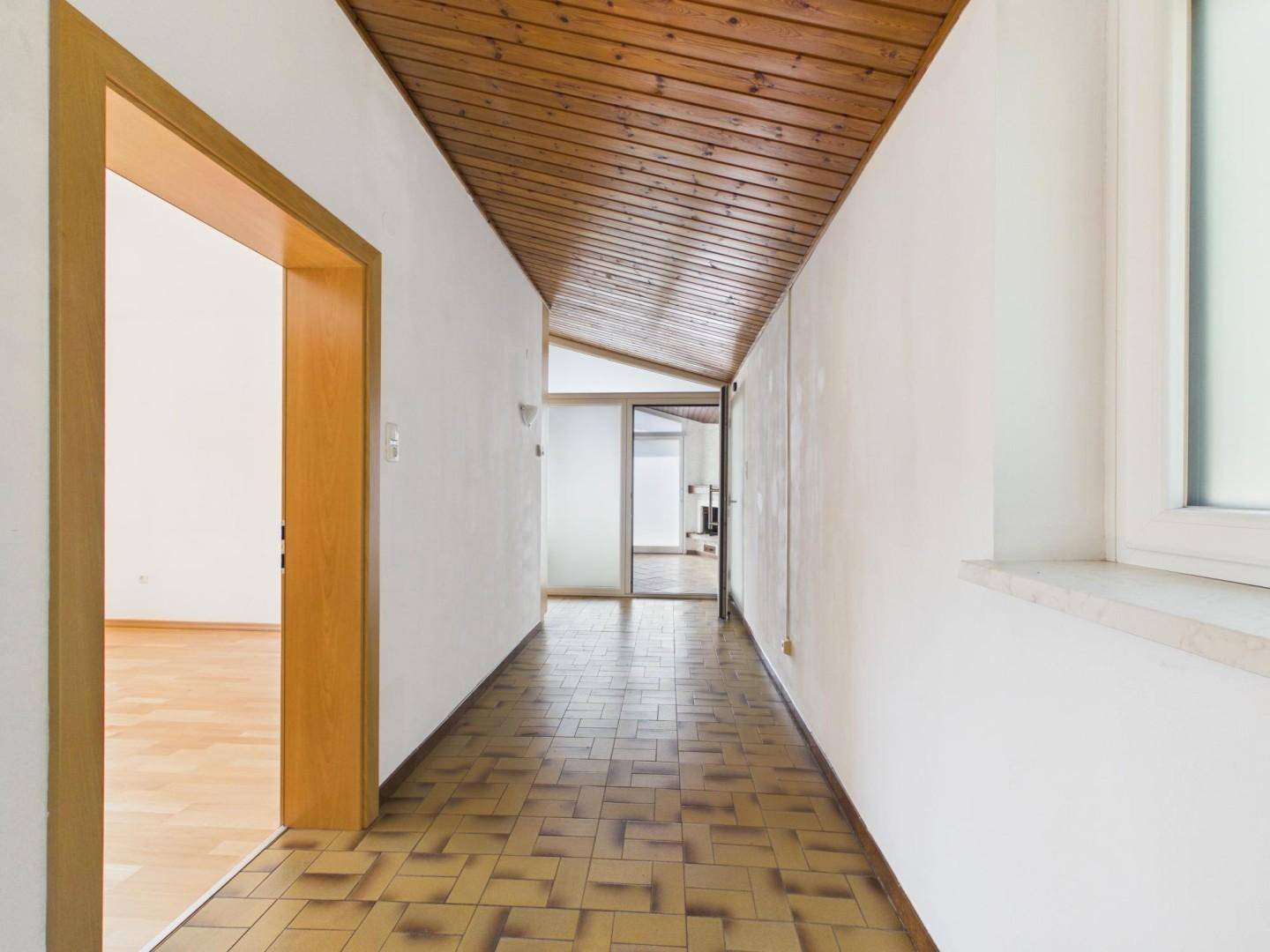 Langer Flur mit gefliestem Boden, Holzdecke und Holztüren, der zu weiteren Räumen führt.