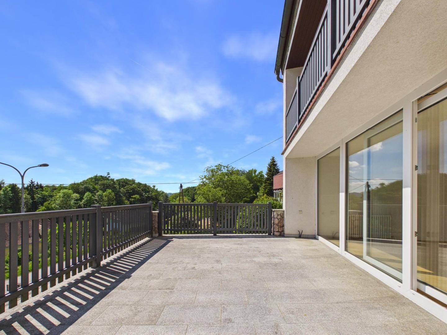 Weitläufige Terrasse mit Steinplatten und Geländer, angrenzend an das Gebäude mit großen Fenstern.