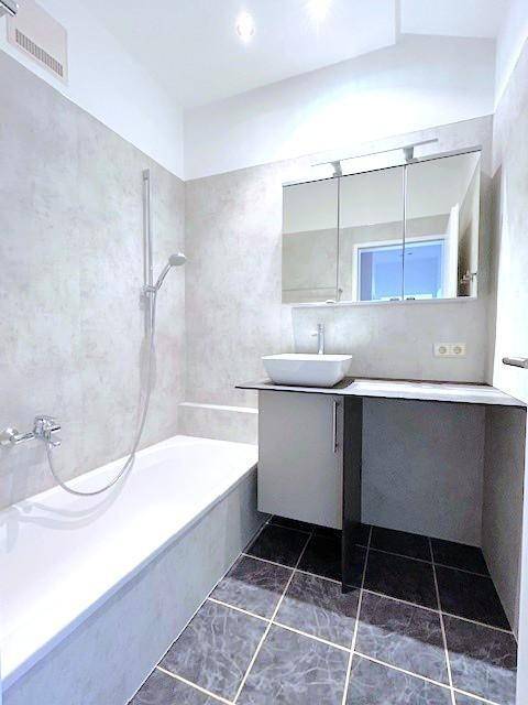 Modernes Badezimmer mit Badewanne, Waschbecken und grauen Fliesen.