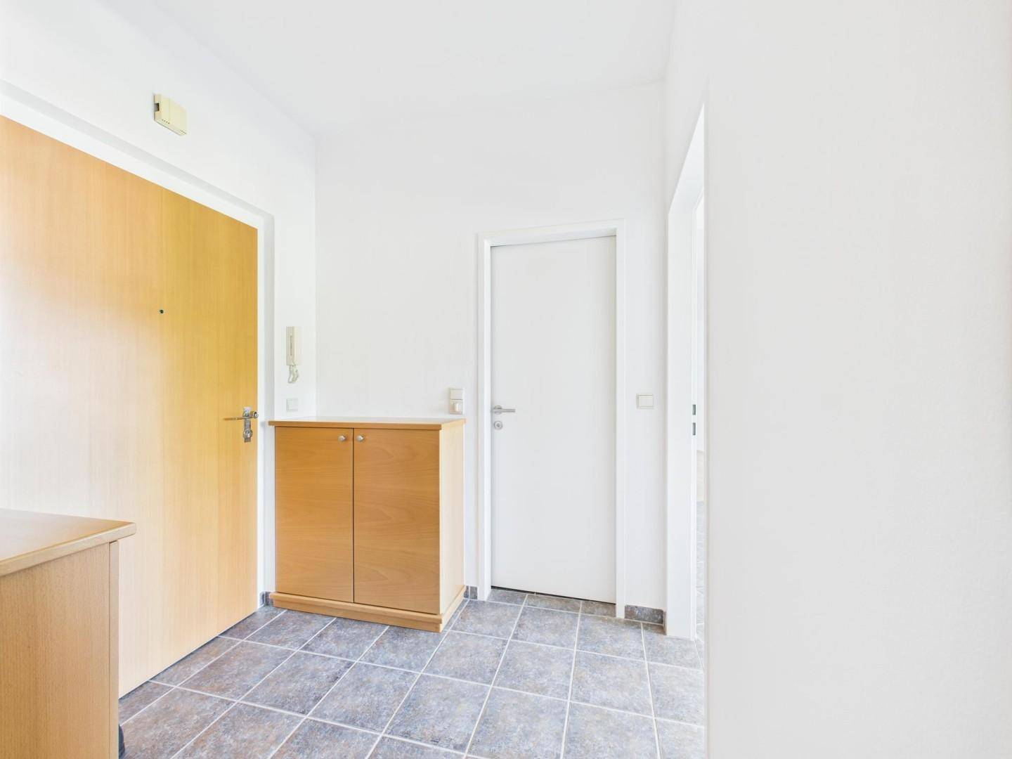 Eingangsbereich mit Fliesenboden und Holzschrank, bietet Zugang zur Wohnung.