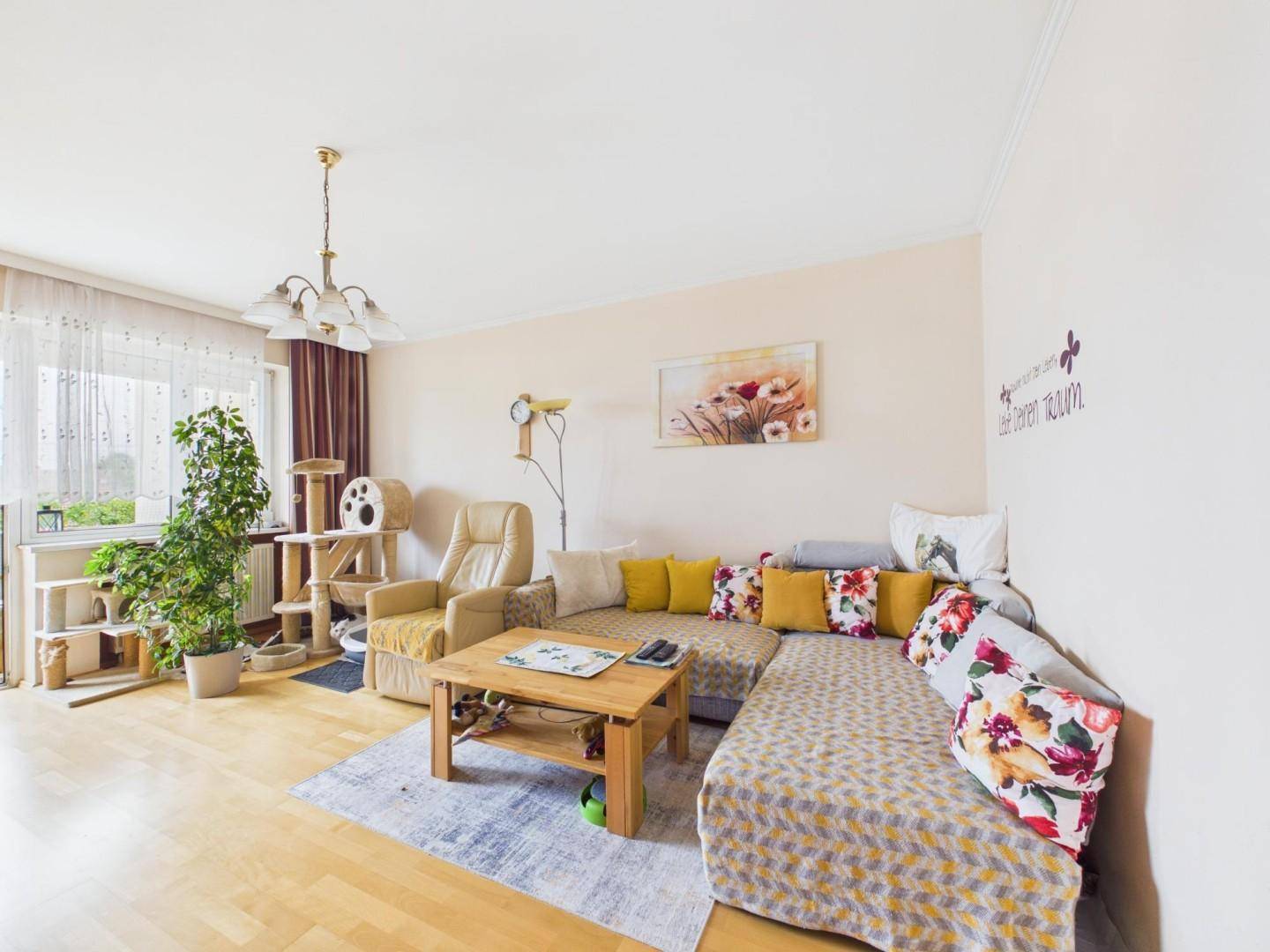 Gemütliches Wohnzimmer mit Sofa, Sessel, Holzboden und Blick ins Grüne durch große Fenster.