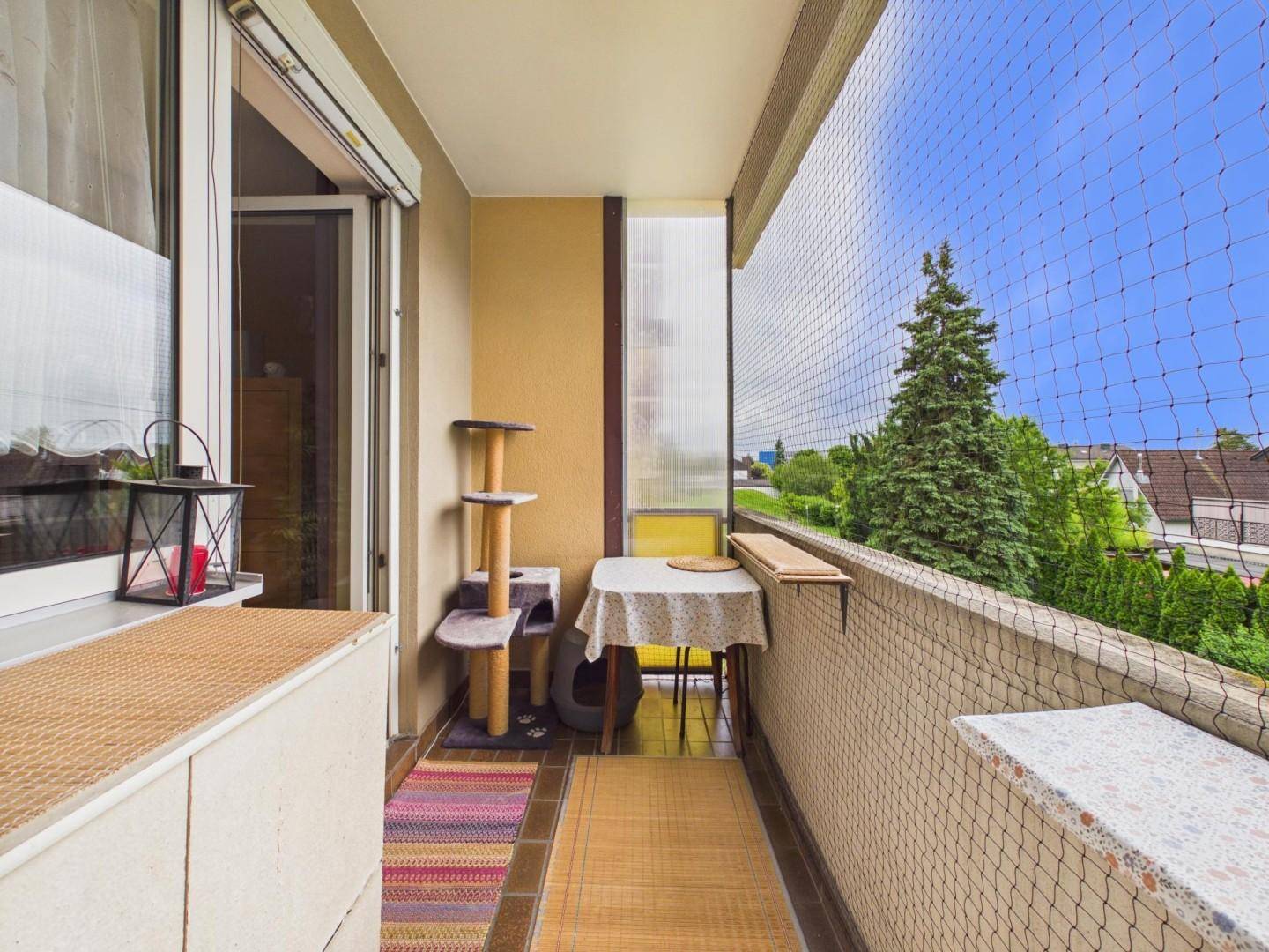 Heller Balkon mit Sicherheitsnetz, kleinem Tisch und weitem Blick ins Grüne.