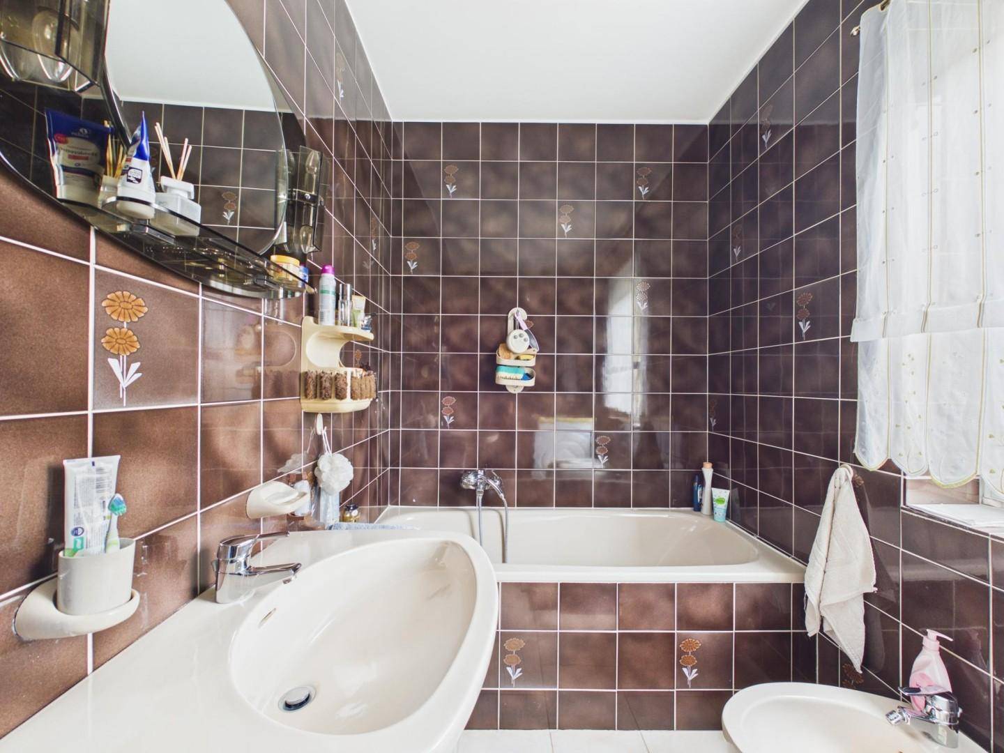Badezimmer im Stil der 80er Jahre mit braunen Fliesen, Badewanne, Waschbecken und Bidet.
