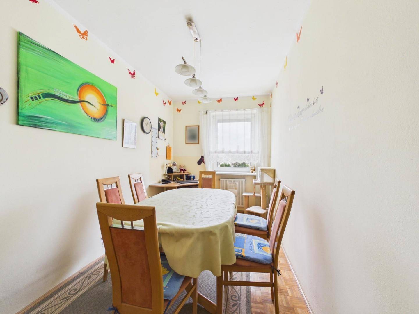 Funktionaler Essbereich mit Holztisch, Stühlen und farbenfrohen Schmetterlingsmotiven an den Wänden.