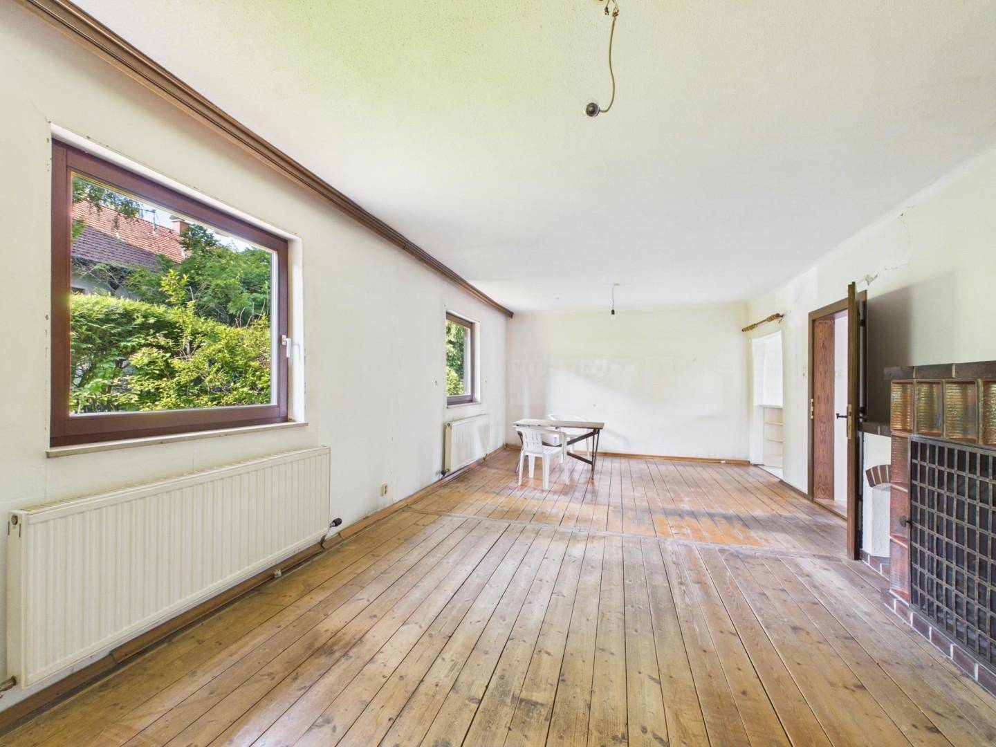 Helles Wohnzimmer mit Holzdielenboden und einem traditionellen Kachelofen als Wärmequelle.