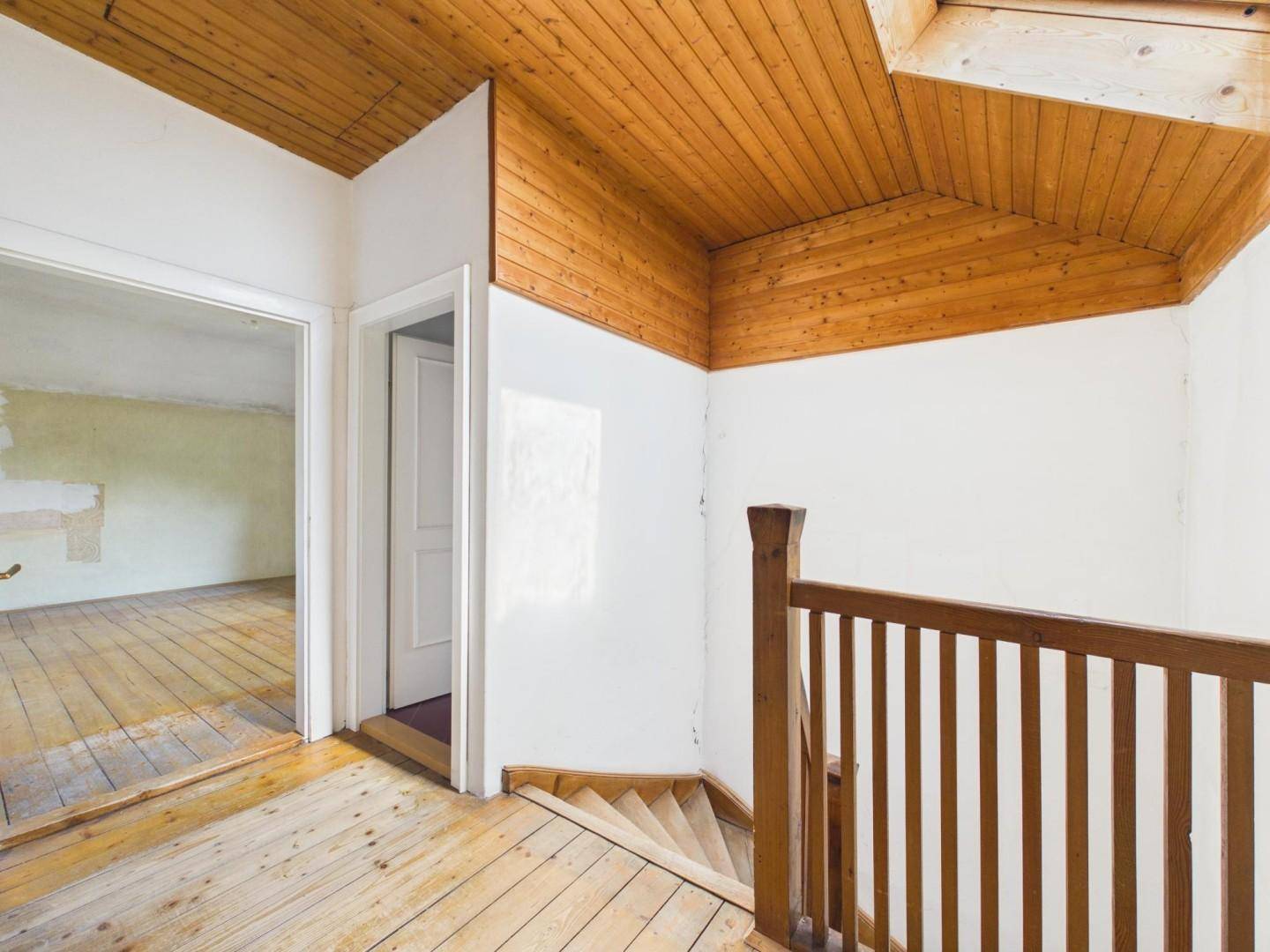 Treppenhaus mit Holzgeländer und Holzdeckenverkleidung, das die Etagen verbindet.