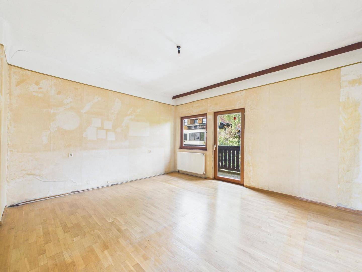 Heller Raum mit Parkettboden und Zugang zu einem Balkon mit traditionellem Holzgeländer.