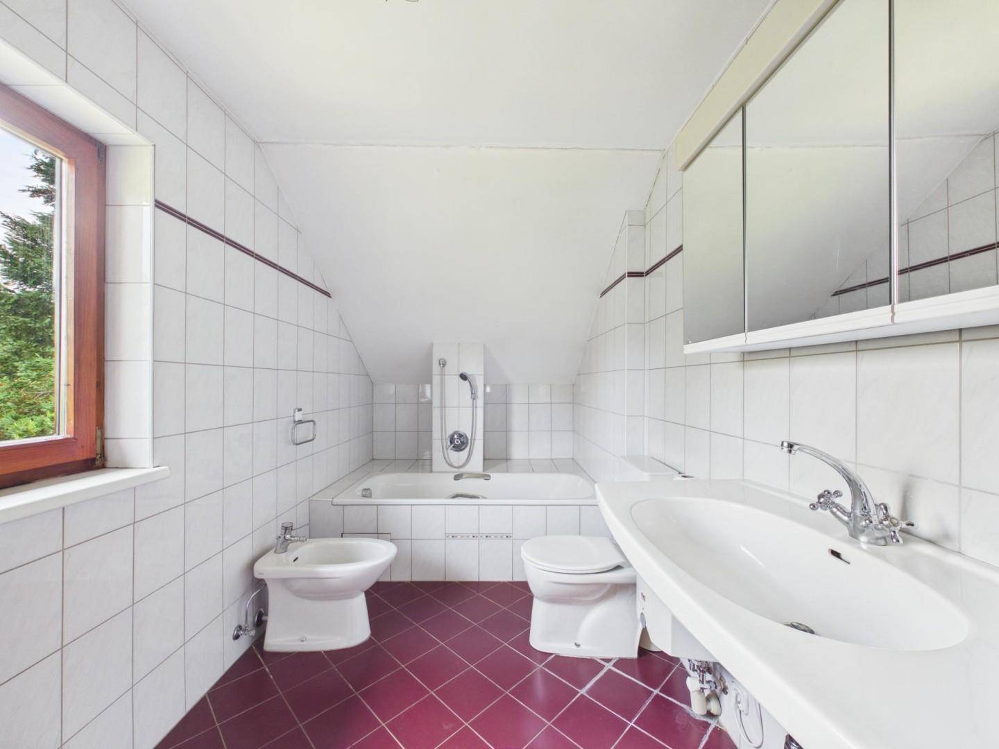 Badezimmer mit Badewanne, Bidet, WC und Waschbecken, gefliest mit roten Bodenfliesen.