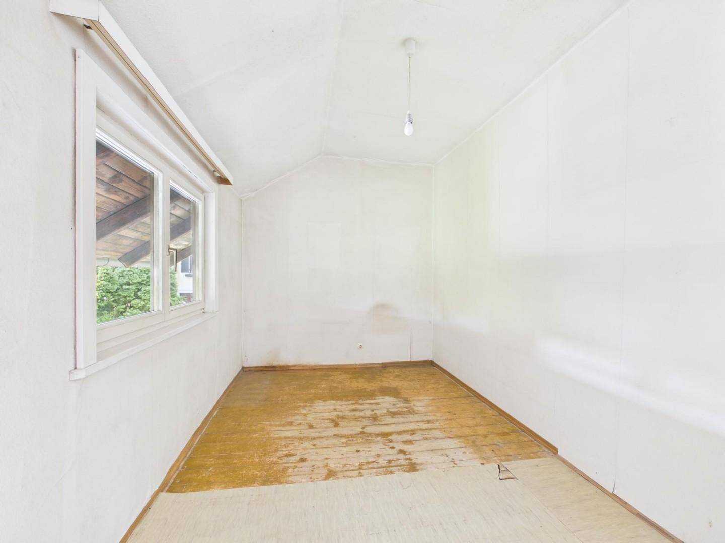 Kleines Zimmer mit Holzdielenboden und Fenster, ideal als Kinder- oder Gästezimmer.