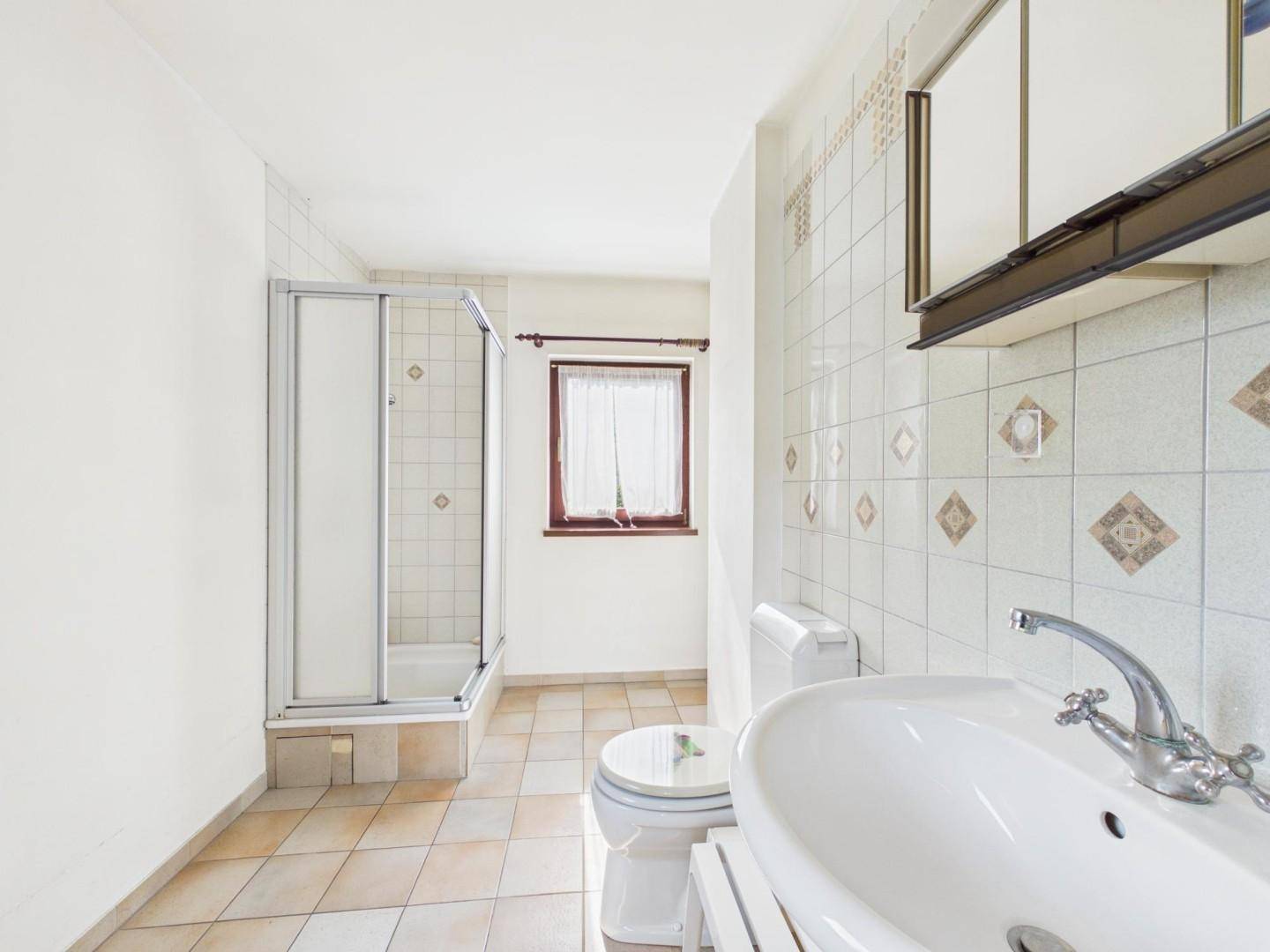 Badezimmer mit Duschkabine, Waschbecken und WC, gefliest in hellen Farbtönen.