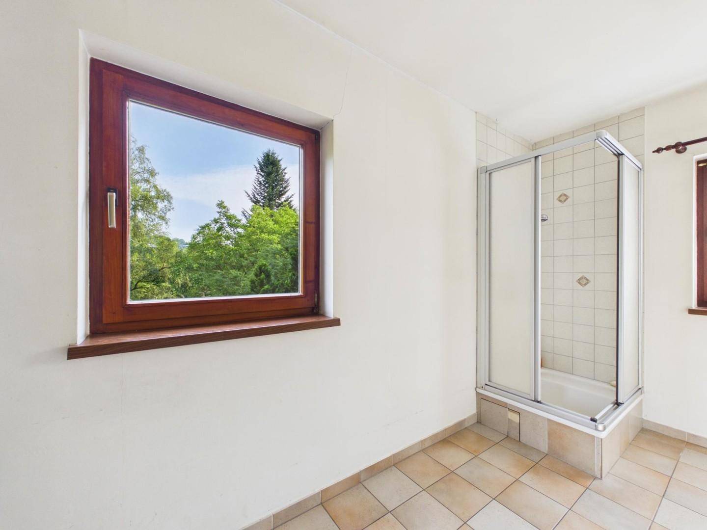 Badezimmer mit Duschkabine und großem Fenster, das viel Tageslicht hereinlässt.