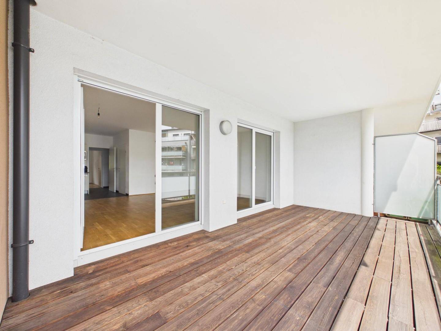 Geräumiger Balkon mit Holzboden und großen Schiebetüren zum Innenbereich.