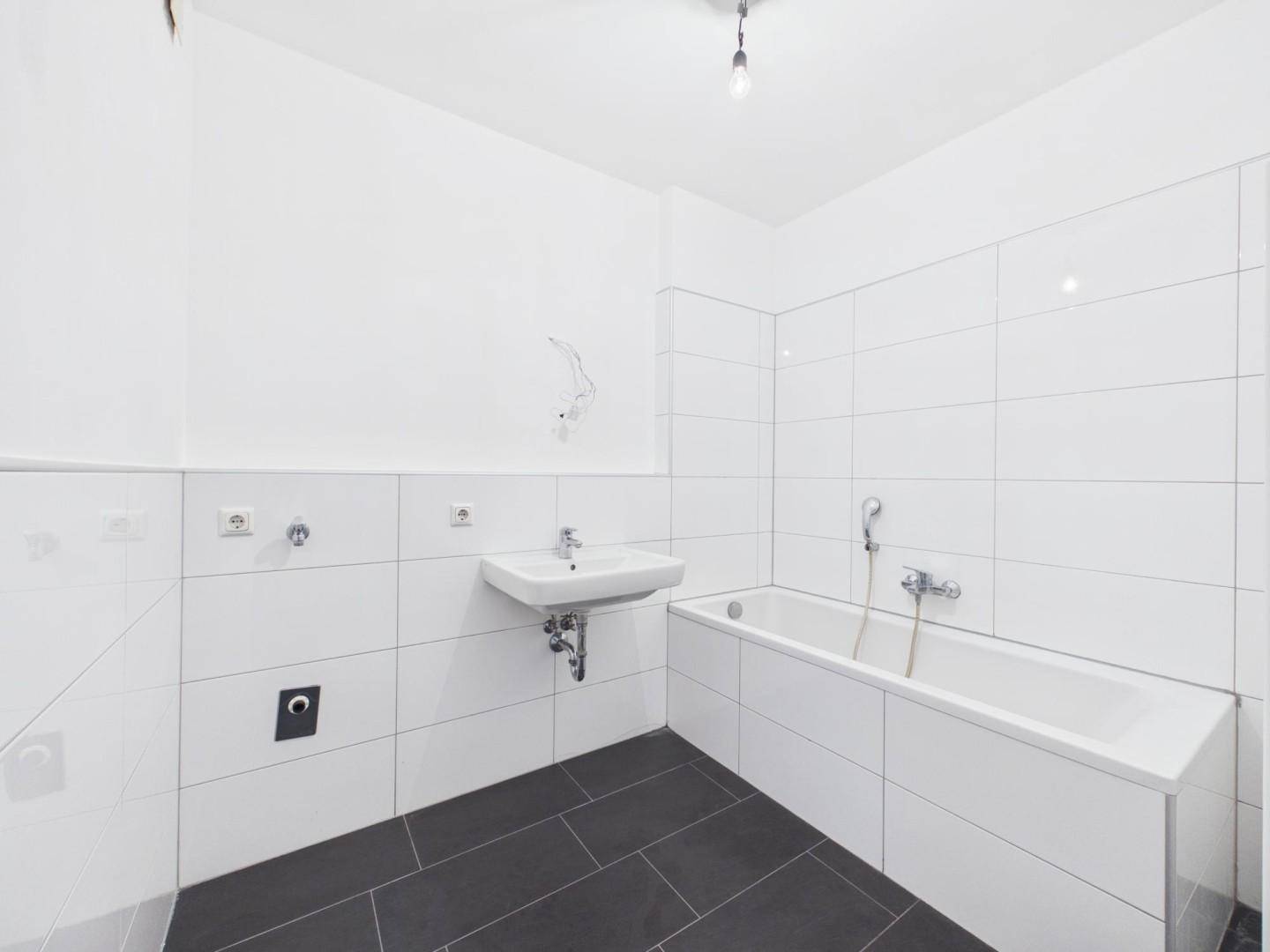 Modernes Badezimmer mit weißen Wandfliesen, dunklem Boden und integrierter Badewanne.