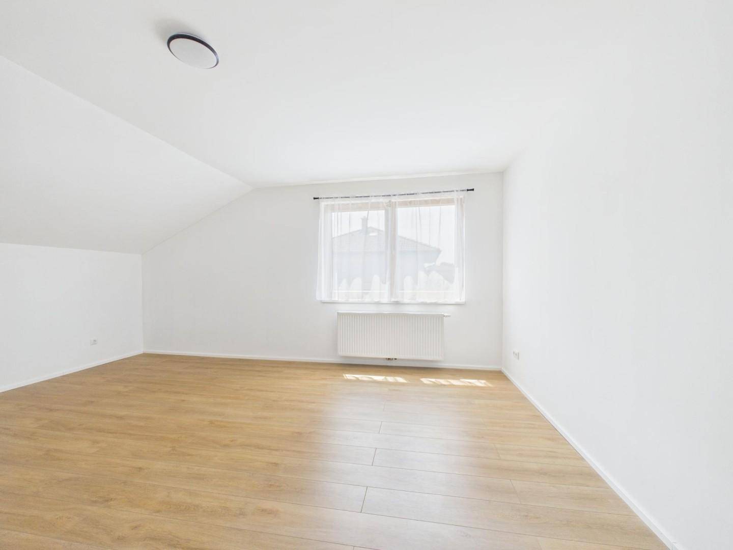 Heller Dachraum mit Laminatboden, weiß gestrichenen Wänden und einem Fenster.