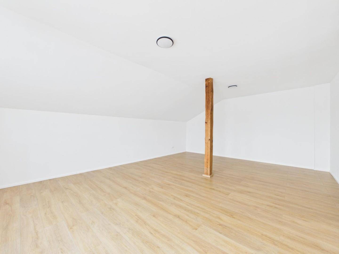 Geräumiges Dachzimmer mit schrägen Wänden, Holzbalken und hellem Laminatboden.