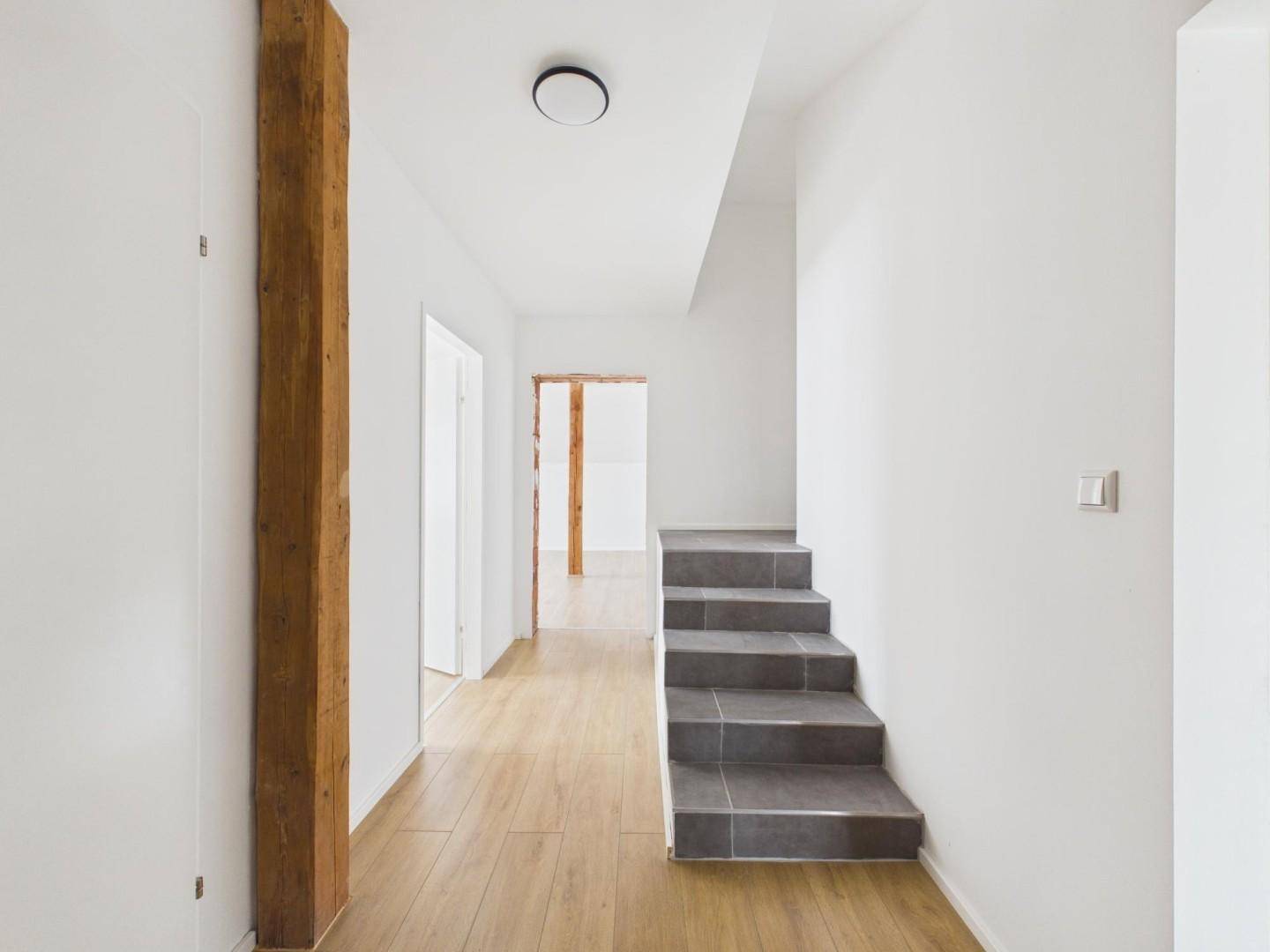 Heller Flur mit Holzpfosten, Laminatboden und Treppe zu den oberen Etagen.