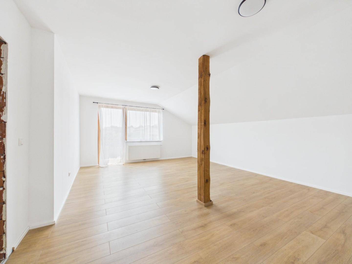 Helles Dachzimmer mit Holzbalken, Laminatboden und Fenster mit Blick ins Grüne.