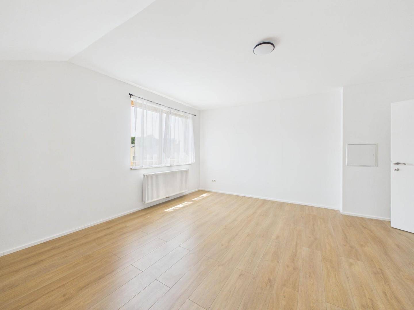 Leeres Dachzimmer mit Laminatboden, weiß gestrichenen Wänden und einem Fenster.