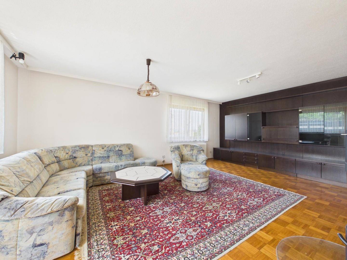 Geräumiges Wohnzimmer mit Parkettboden, großer Couch und traditionellem Teppich.