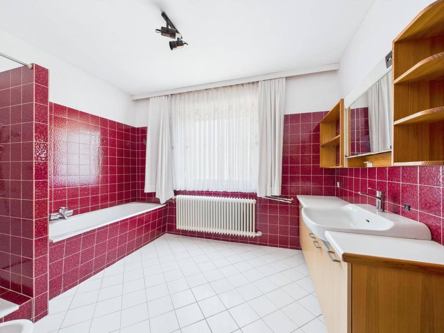 Badezimmer mit roten Fliesen, Badewanne, Doppelwaschbecken und Fenster.