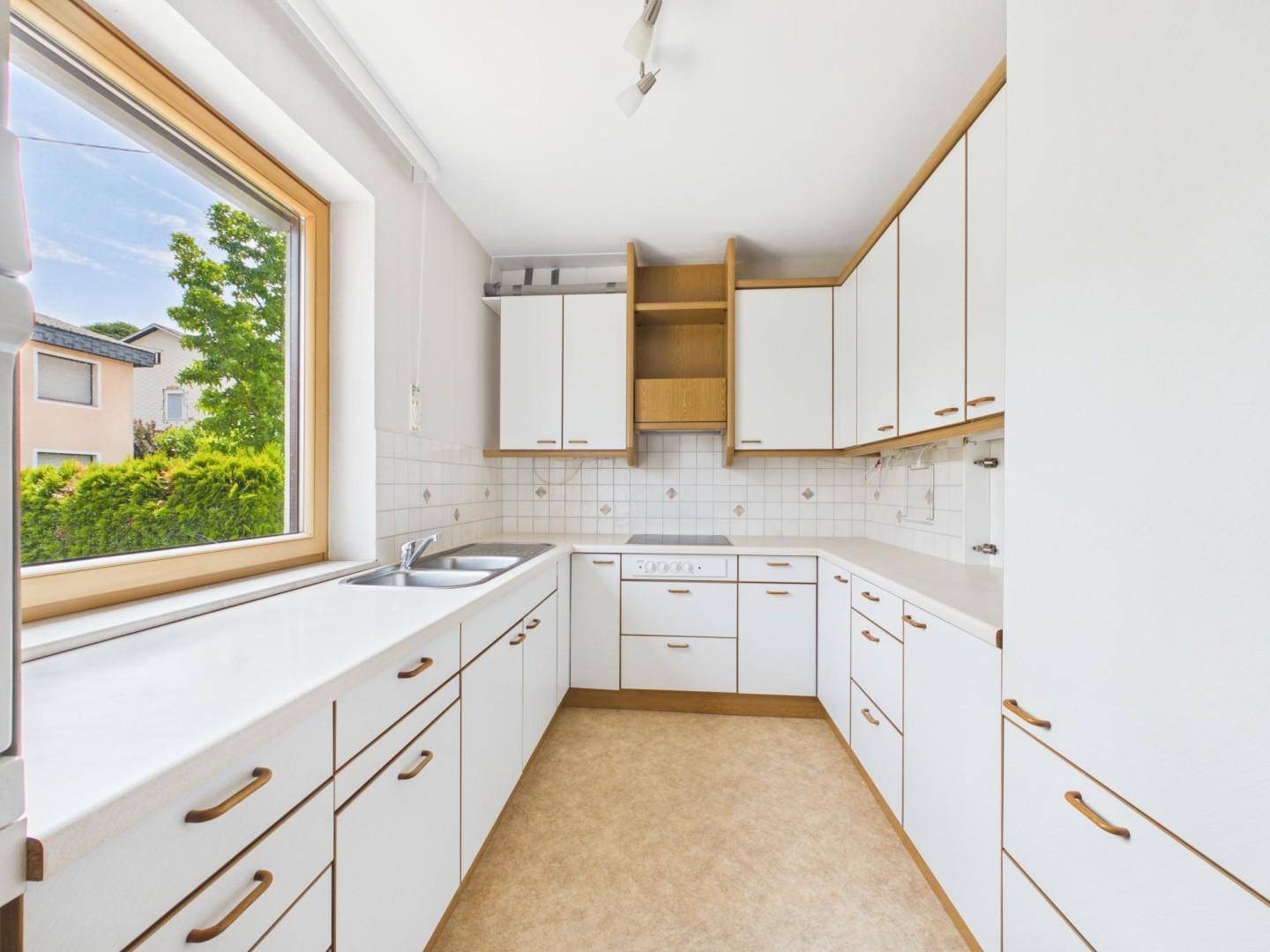 Helle Küche mit weißen Einbauschränken, Fenster und Blick in den Garten.