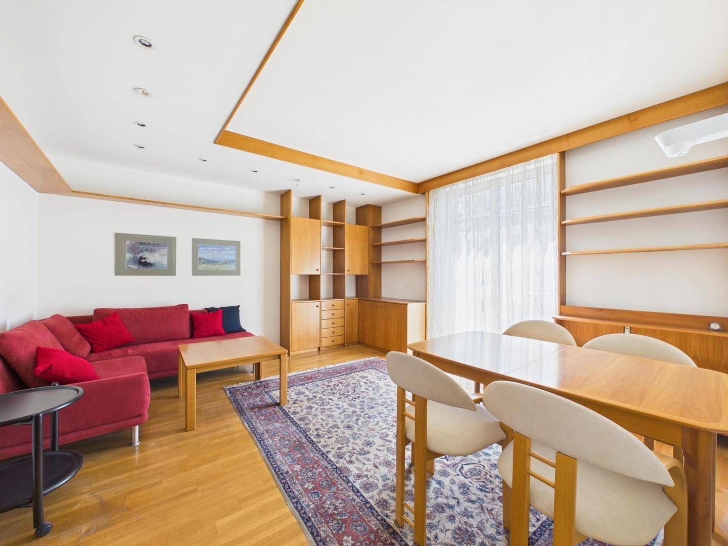 Heller Wohn- und Essbereich mit Holzmöbeln, rotem Sofa und Parkettboden.