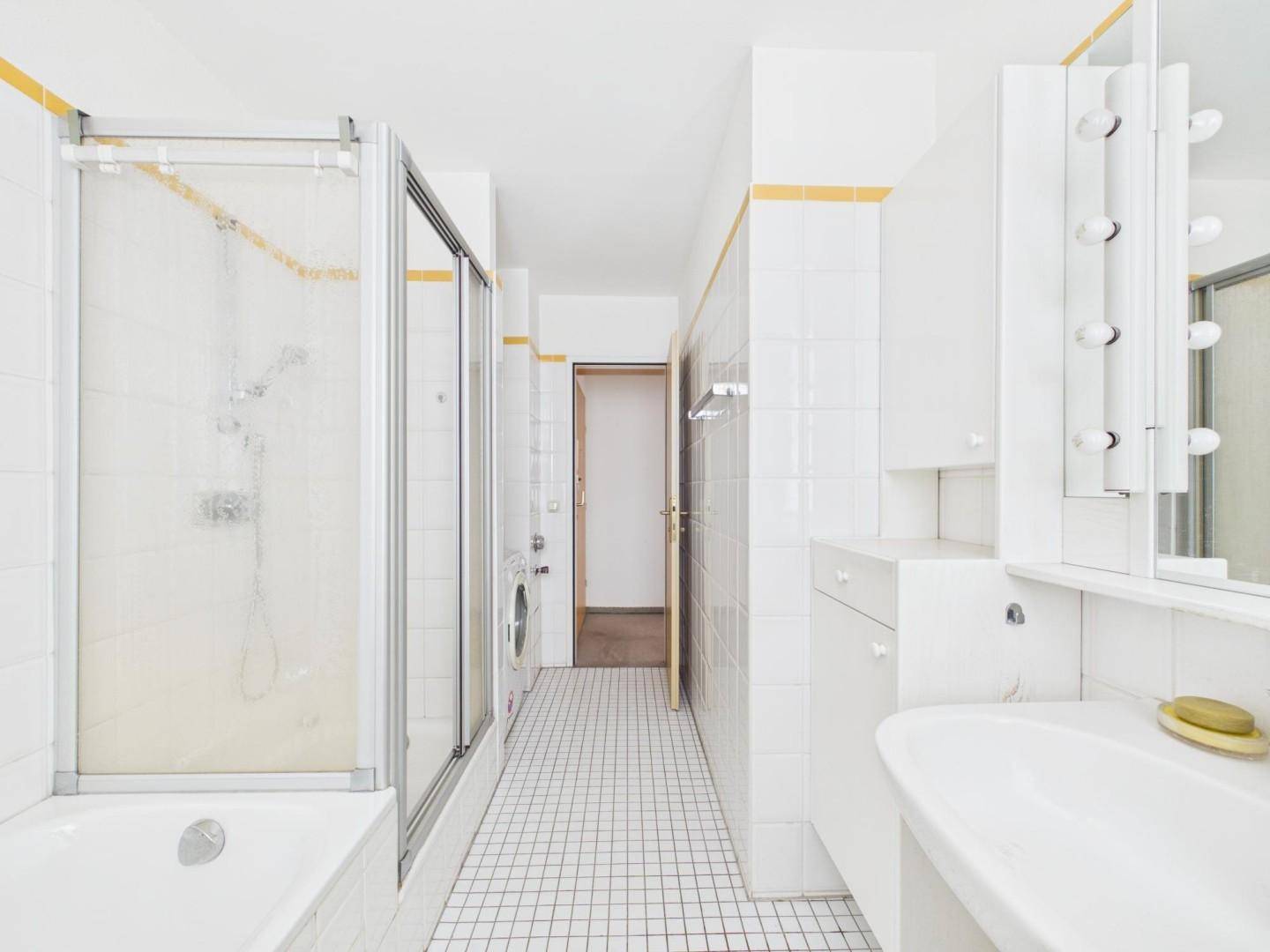 Weiß gefliestes Badezimmer mit Badewanne, Dusche und Waschbecken.