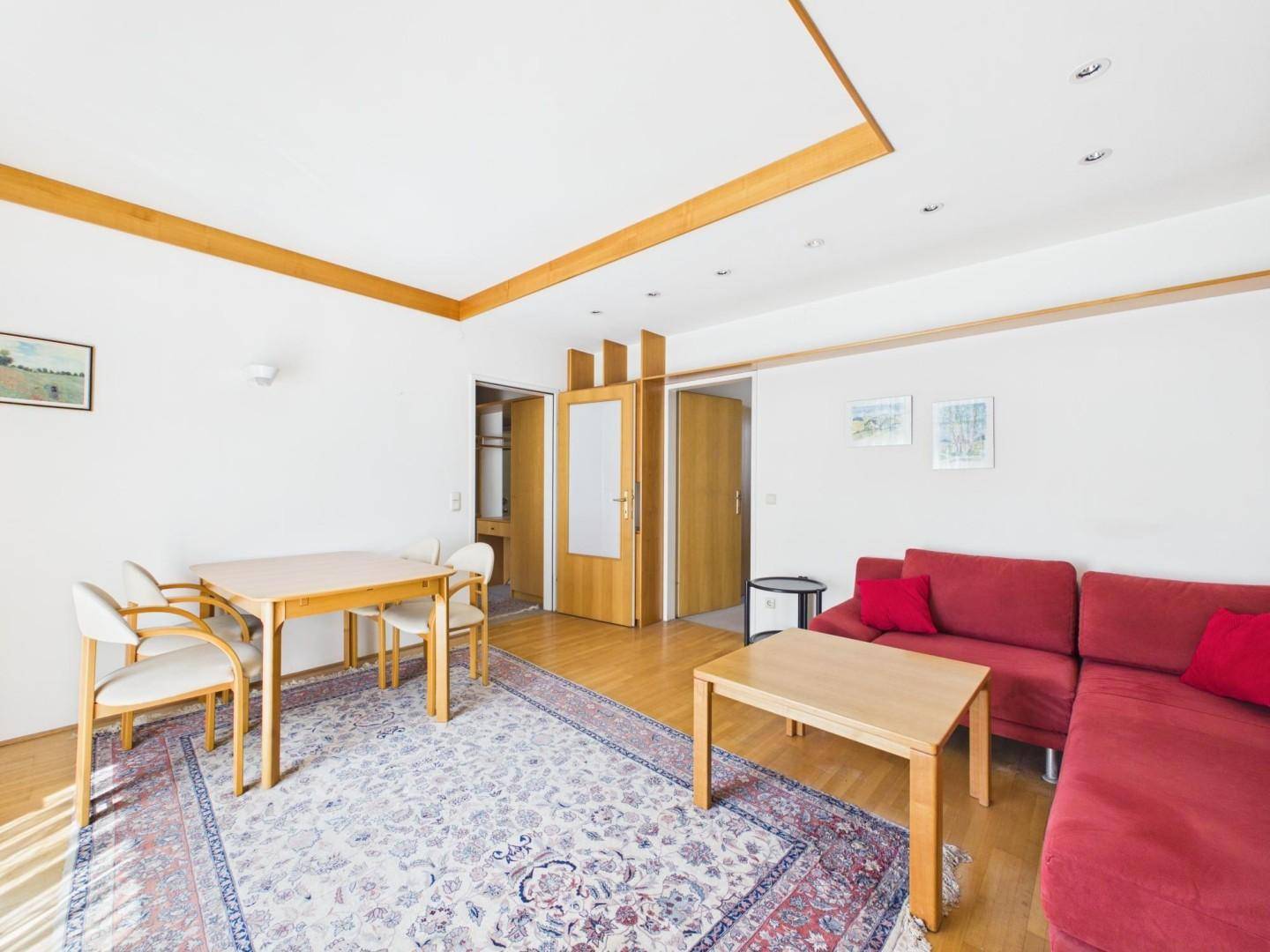 Geräumiger Wohn- und Essbereich mit Holzboden, rotem Sofa und Esstisch.