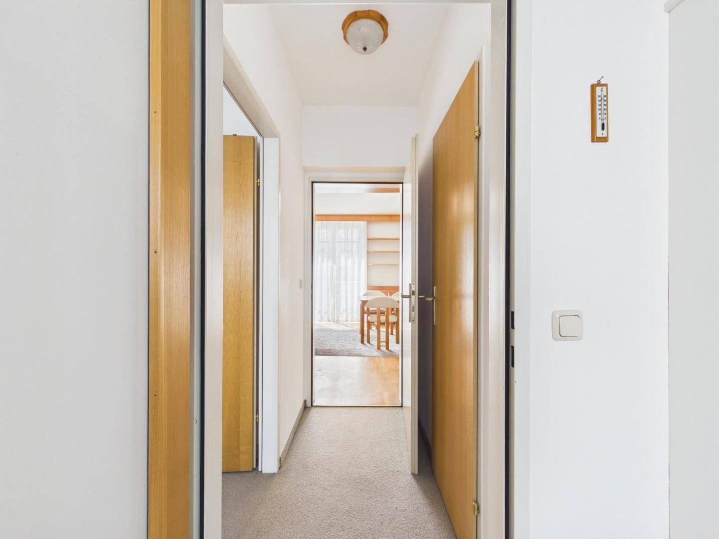 Langer Flur mit Teppichboden und Holztüren, der zu weiteren Räumen führt.