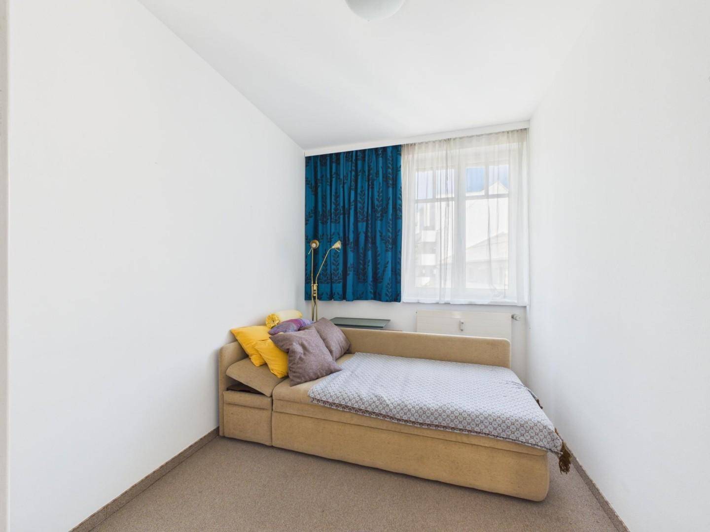 Kleines Schlafzimmer mit Schlafsofa, blauen Vorhängen und Teppichboden.